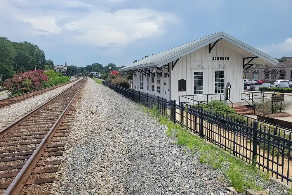 Acworth Depot, a white train depot beside railroad tracks and a black iron fence in Acworth, Georgia