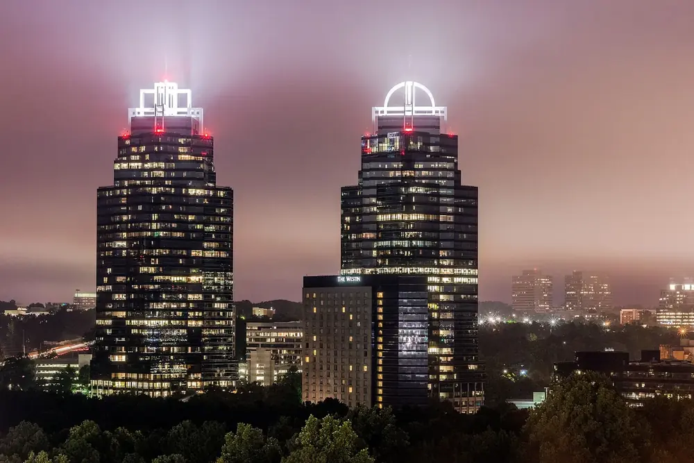 The twin King and Queen office towers lit at night above fog and trees in Sandy Springs, Georgia